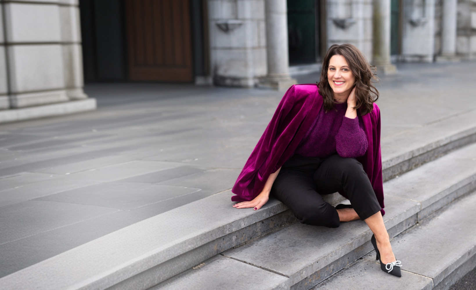Carly Clark Zimmer seated on stone steps in a magenta velvet jacket