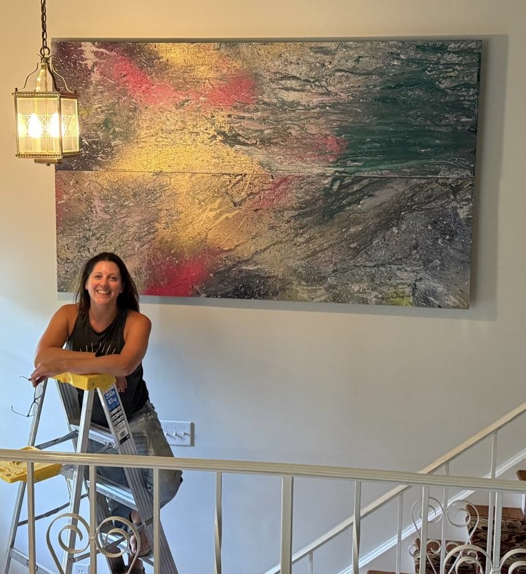 Carly smiling beside one of her large abstract paintings